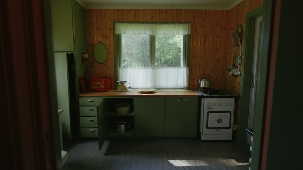 Dated kitchen with original cabinets and worn floorboards in a house being sold as is